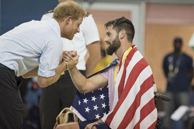 rince Harry shakes hands with Army veteran Sgt. Stefan Leroy while his dog looks on during swim finals at the Invictus Games in Toronto, Sept. 29, 2017. Prince Harry, who served in Afghanistan, established the games in 2014. (DoD/Roger L. Wollenberg)
