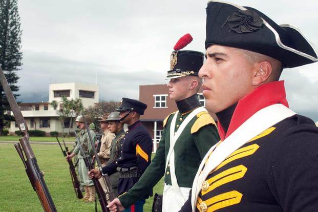 Marines and sailors stand in formation dressed up in historical uniforms. 