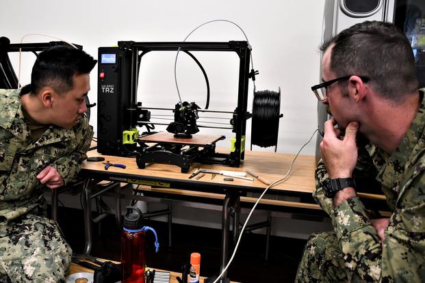 Sailors watch a 3D printer.