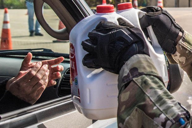 A soldier hands off gallons of milk at a food distribution point.