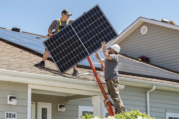 Wyatt Whelan, left, and Eric Roberts, both PosiGen install supervisors, move a photovoltaic panel to a roof in the Dover Family Housing community at Dover Air Force Base, Delaware.