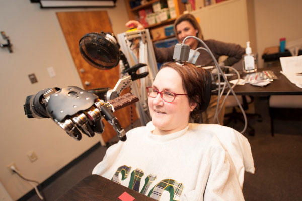 Jan Scheuermann, who has quadriplegia, brings a chocolate bar to her mouth using a robot arm she is guiding with her thoughts. (Photo by University of Pittsburgh Medical Center)