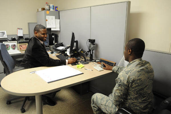 Service member having a discussion at a desk in front of a computer.