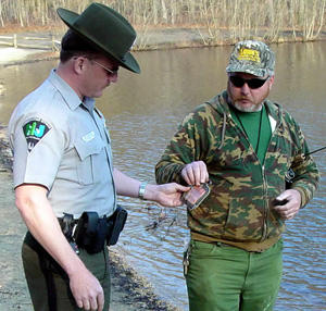 Conservation officer checking license by a lake.