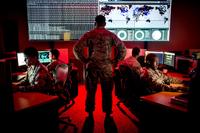 A cyber warfare operations officer watches service members analyze log files at Warfield Air National Guard Base.