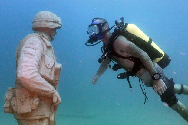 A veteran scuba dives around a memorial. 