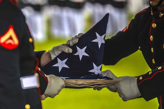 Marine Corps Body Bearers fold the National Flag during a full honors funeral at Arlington Cemetery.