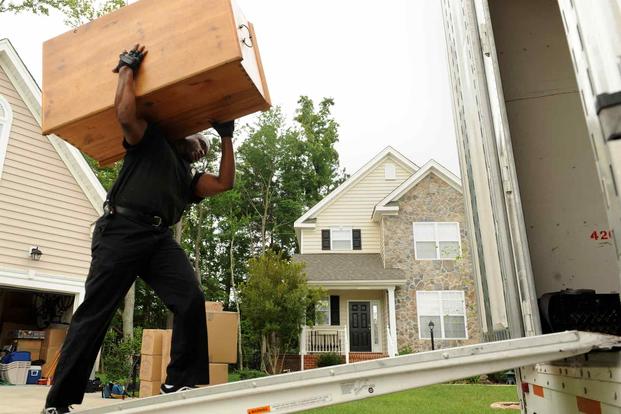 A mover loads a heavy dresser into a moving van. 