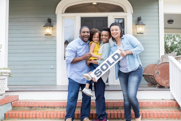 family with sold sign in front of house