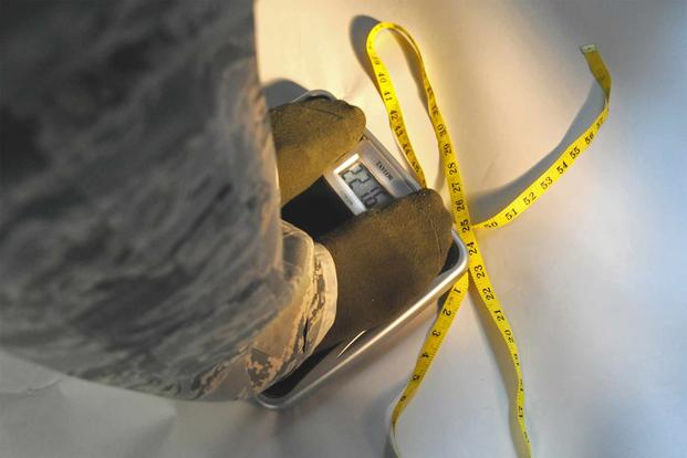 An airman checks his status with a scale and a tape measure. 