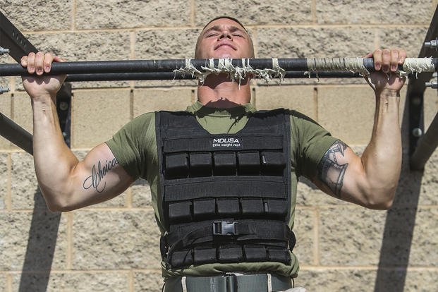 A Marine performs pull-ups while wearing a weight vest.