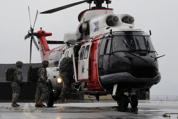 Army explosive ordnance disposal technicians load onto an Icelandic AS332 Super Puma helicopter.