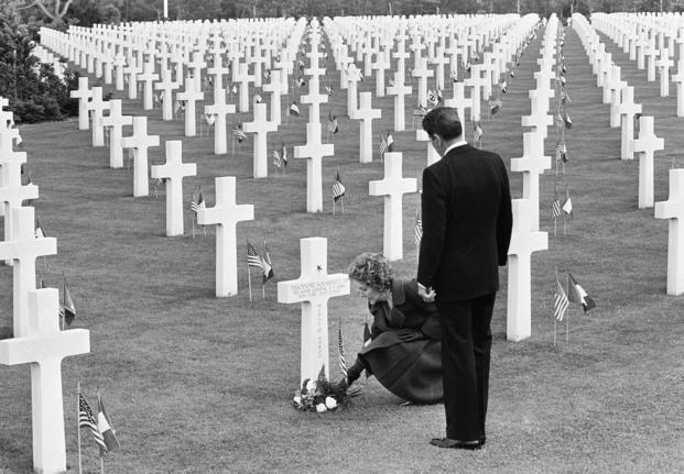 Nancy Reagan puts down a bunch of flowers at the grave of Theodore Roosevelt Jr. at the Normandy American Cemetery at Omaha Beach, France, as Pres. Ronald Reagan stands behind her.