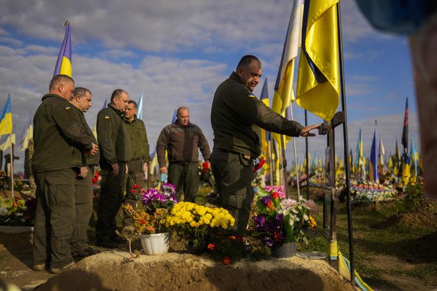 Ukrainian servicemen place flowers on the grave of a recently killed fellow soldier in a cemetery.