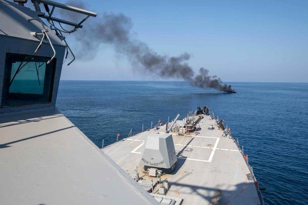 The guided-missile destroyer USS Nitze approaches a burning motorboat.