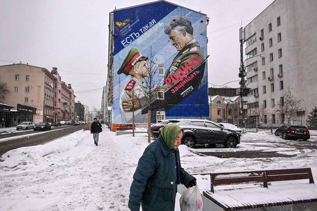 A pedestrian walks past a mural depicting a Russian General and a cadet.