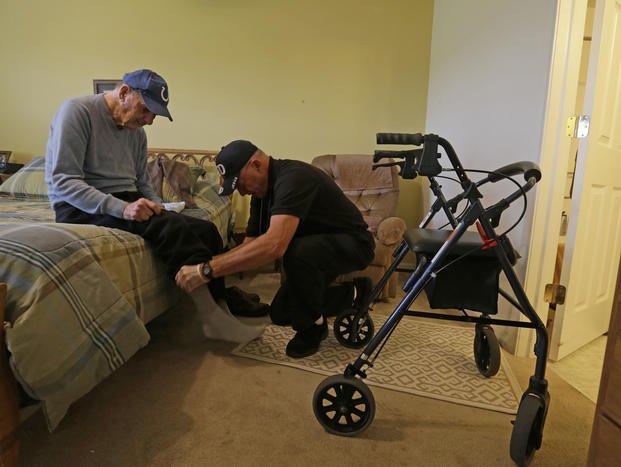 caregiver Warren Manchess helping Paul Gregoline, a WWII veteran, with his shoes and socks