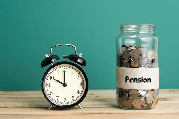 An alarm clock sits on a table next to a jar of coins labeled Pension