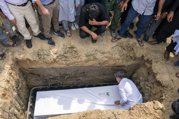 Friends and family watch as the body of Nasrat Ahmad Yar, 31, is placed into a grave during a funeral service