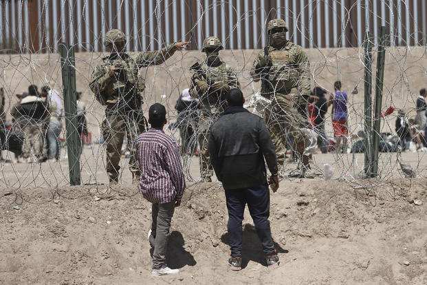 Migrants listen to members of the Texas National Guard before passing through a razor wire barrier from Ciudad Juarez, Mexico into El Paso, Texas, Thursday.