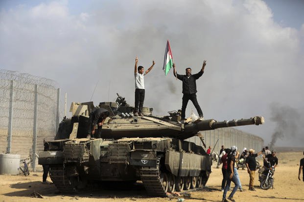 Palestinians wave their national flag by a destroyed Israeli tank.
