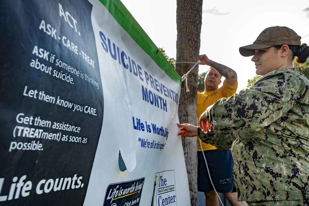 Two Navy sailors a raise a banner for Suicide Awareness Month