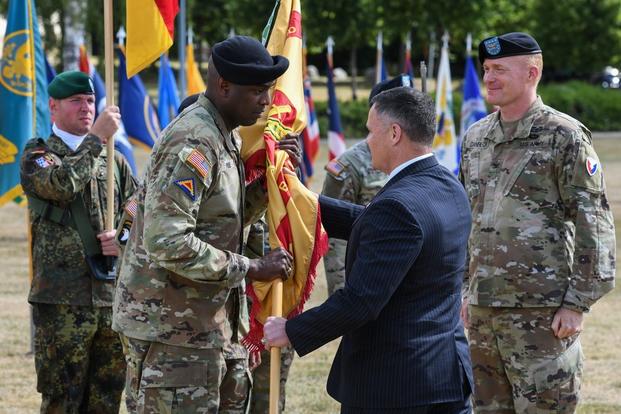 Mr. Tommy Mize, center, Director, Installation Management Command Directorate-Europe, passes the unit colors to U.S. Army Col. Kevin A. Poole, the incoming commander of U.S. Army Garrison Bavaria, during a change of command ceremony at Grafenwoehr Training Area, Germany, July 12, 2022.