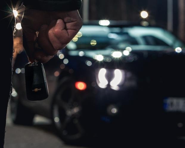 A person holds a car key in front of a car.