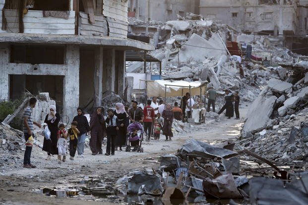 Displaced Palestinians walk next to sewage flowing into the streets.