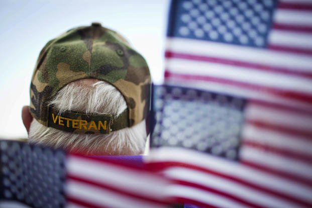 A man wears a veterans hat surrounded by flags as he attends a Veterans Day parade Tuesday in Montgomery, Ala. 