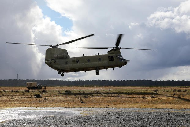 A CH-47 Chinook helicopter hovers over the ground in preparation to sling-load an M777 155 mm howitzer to send to a secondary firing position on Joint Base Lewis McChord, Wash.