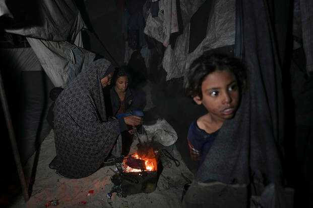 Woman displaced with her children checks the fire next to their tent in the Gaza Strip.