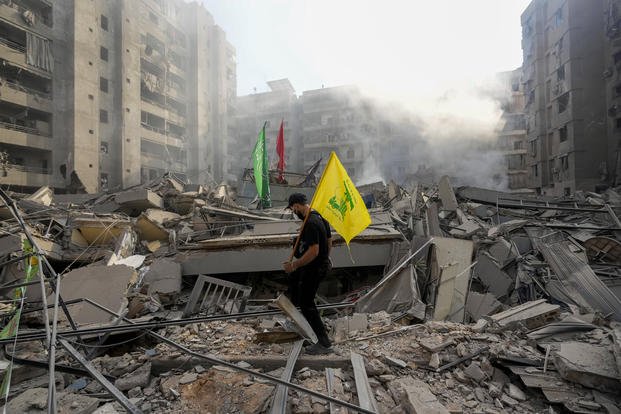 A man carries a Hezbollah flag as he walks on the rubble of his destroyed apartment.