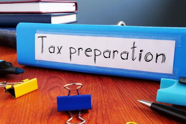 A blue binder features a handwritten label on its spine, "Tax preparation," set on a wood desk amid office supplies.