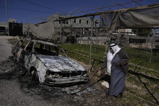 Palestinian stands beside a torched car in the West Bank