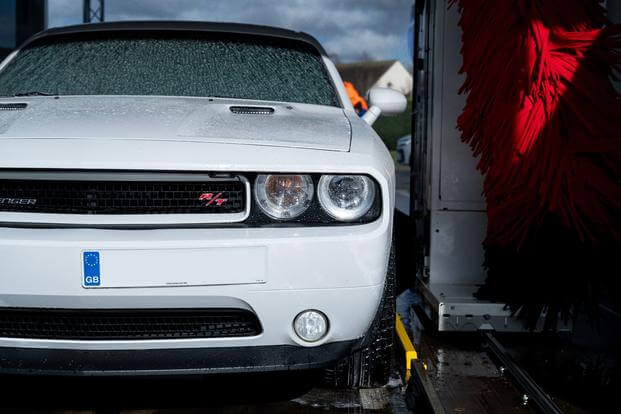 The front end of a white Dodge Charger appears emerging from a car wash.