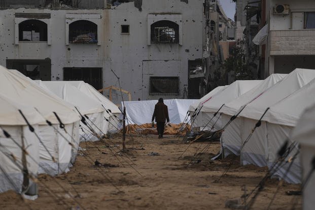 A man walks between tents for displaced Palestinians next to destroyed buildings