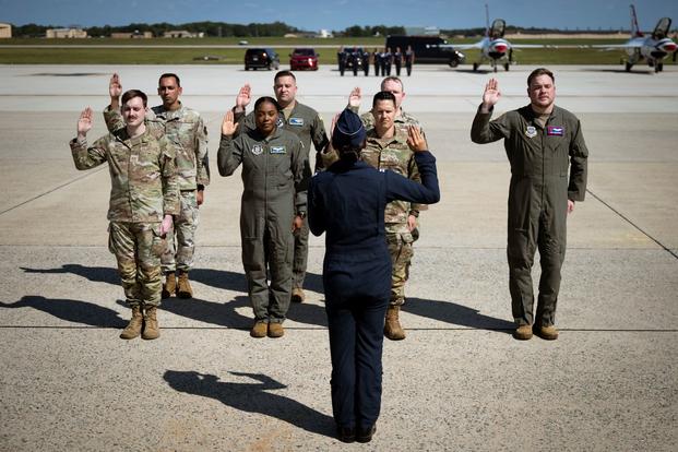 Air Force members in flights suits and camouflage raise their right hands to reenlist.