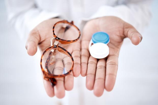 One hand holding glasses, one holding a contact case.