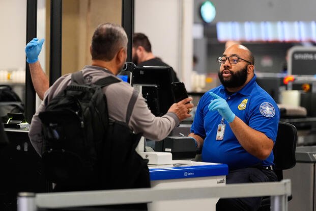 A TSA agent assists a traveler at a security checkpoint at the Dallas Fort Worth International Airport, at DFW Airport, Texas, Friday, Nov. 21, 2025. (AP Photo/Tony Gutierrez)