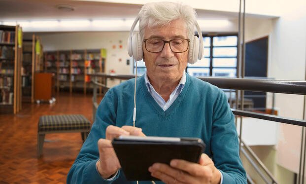 Gentleman in a library listening to an audiobook on a tablet with headphones. Photo credit: Kampus Production, image made available under creative commons and fair use. 