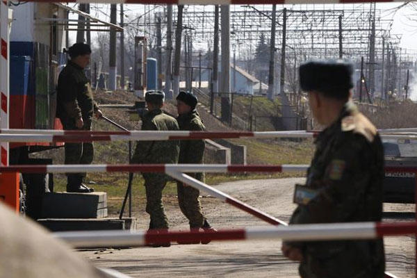 In this photo taken Monday, March 24, 2014, a Ukrainian border guard, right, and Russian border guards, background, stand at the crossing between Ukraine and Russia in the village of Vyselki, eastern Ukraine. (AP Photo/Sergei Grits)