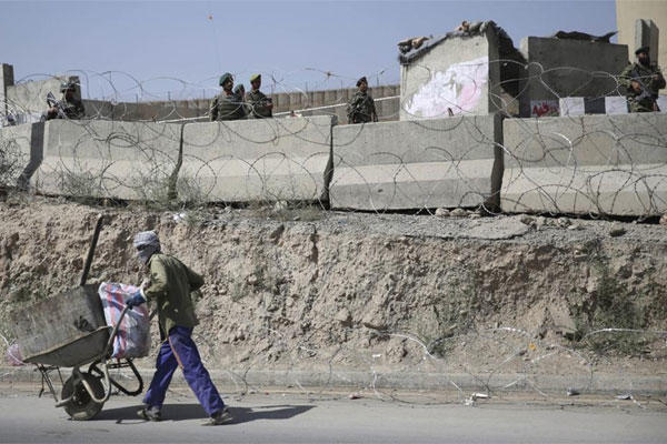 An Afghan laborer walks past a gate of Camp Qargha as Afghanistan National Army soldiers stand guard, west of Kabul, Afghanistan, Tuesday, Aug. 5, 2014. (AP Photo/Massoud Hossaini)