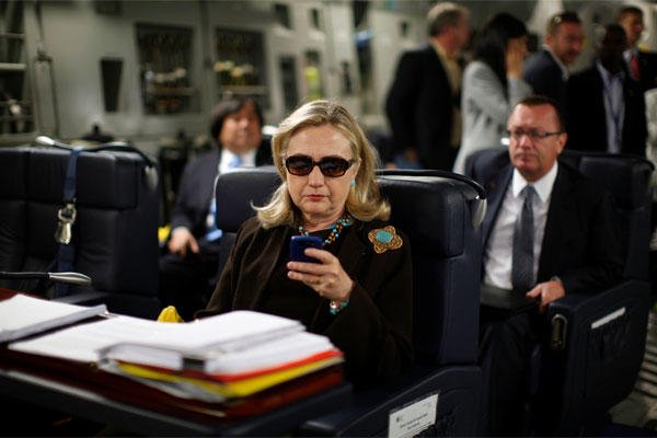 In this Oct. 18, 2011, file photo, then-Secretary of State Hillary Rodham Clinton checks her Blackberry from a desk inside a C-17 military plane upon her departure from Malta bound for Tripoli, Libya. (AP Photo/Kevin Lamarque, Pool, File)