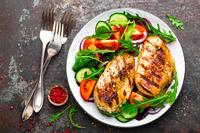 Grilled chicken breast and fresh vegetable salad of tomatoes, cucumbers and arugula leaves.