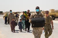 A Marine carries an Afghan evacuee's luggage as they prepare to board an airplane in Qatar.