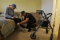 caregiver Warren Manchess helping Paul Gregoline, a WWII veteran, with his shoes and socks