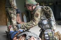 A service member in combat gear attaches a medical dummy to a stretcher.