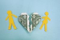 Paper cutouts representing a man and a woman are arranged on either side of a dollar bill that's been folded into the shape of a heart and cut in jagged pieces