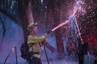 A California Department of Forestry and Fire Protection firefighter hoses down hot spots from the Anzar Fire near Aromas, Calif.